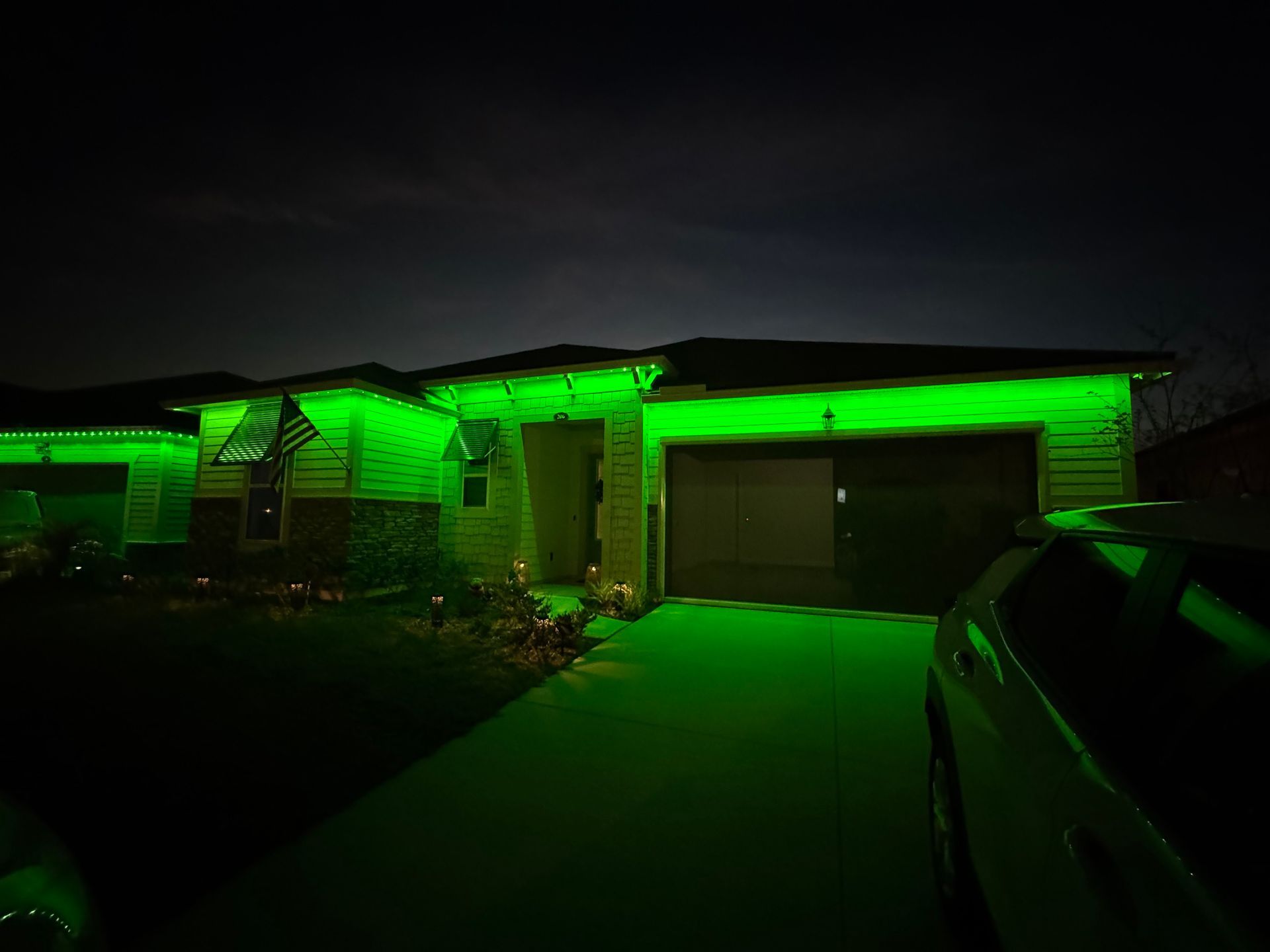 House with green lights illuminating the roofline and driveway at night.