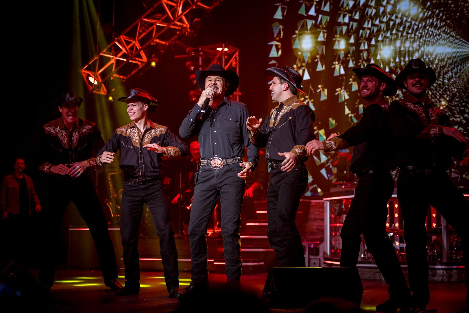a group of men in black outfits with cowboy hats are on stage while the man in the center is singing into a microphone 
