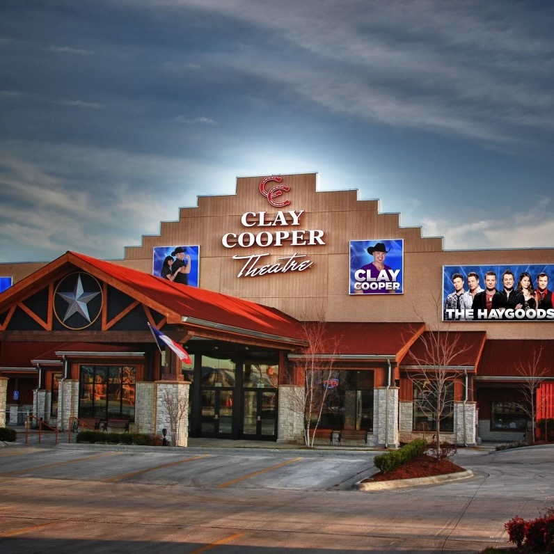 The Clay Cooper Theatre building with tan siding, a red roof, and posters of Clay Cooper and The Haygoods.