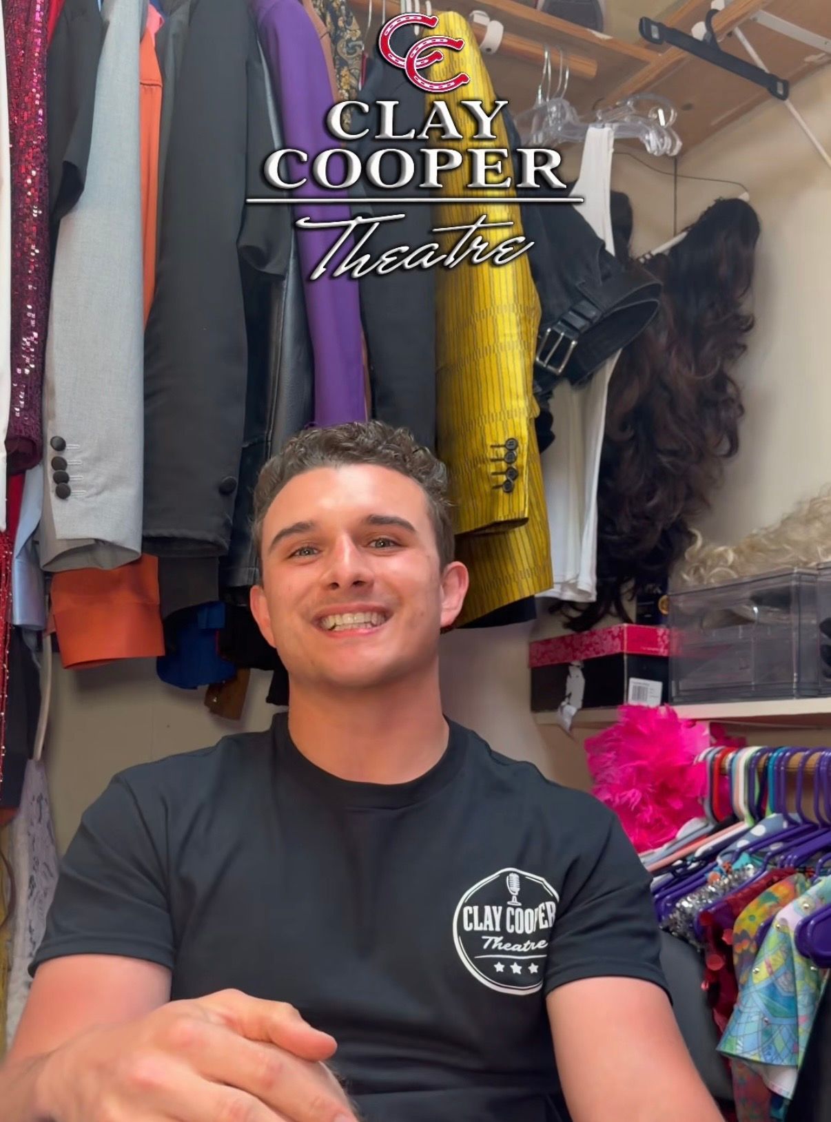 screenshot of a young man sitting in a chair smiling with the Clay Cooper Theatre logo above his head, appears to be in a dressing room full of costumes