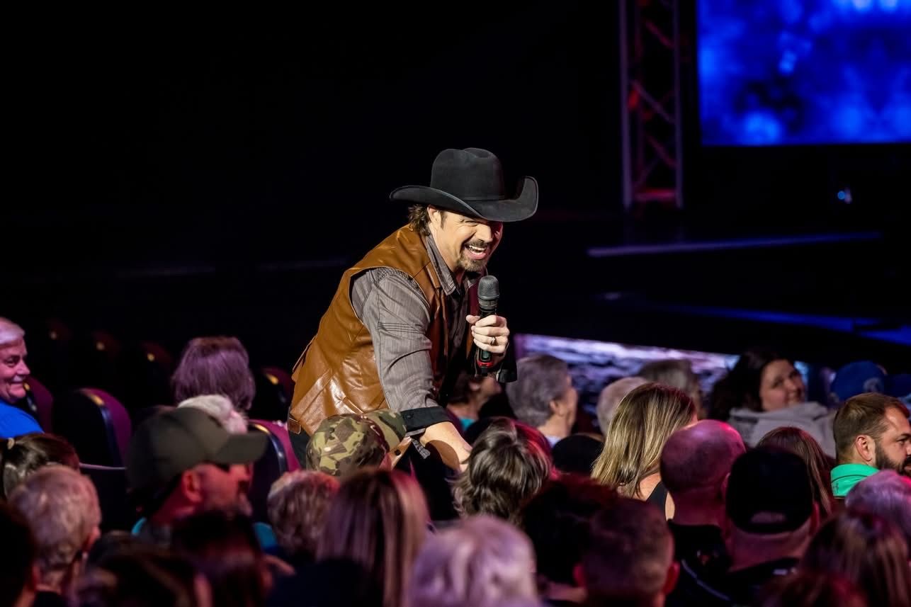 man in cowboy hat with microphone shaking hands with audience members 