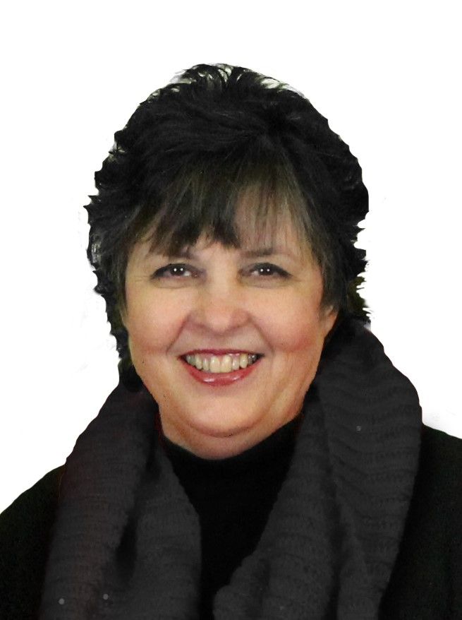 A person with dark, short hair and a black scarf smiling at the camera against a white background.