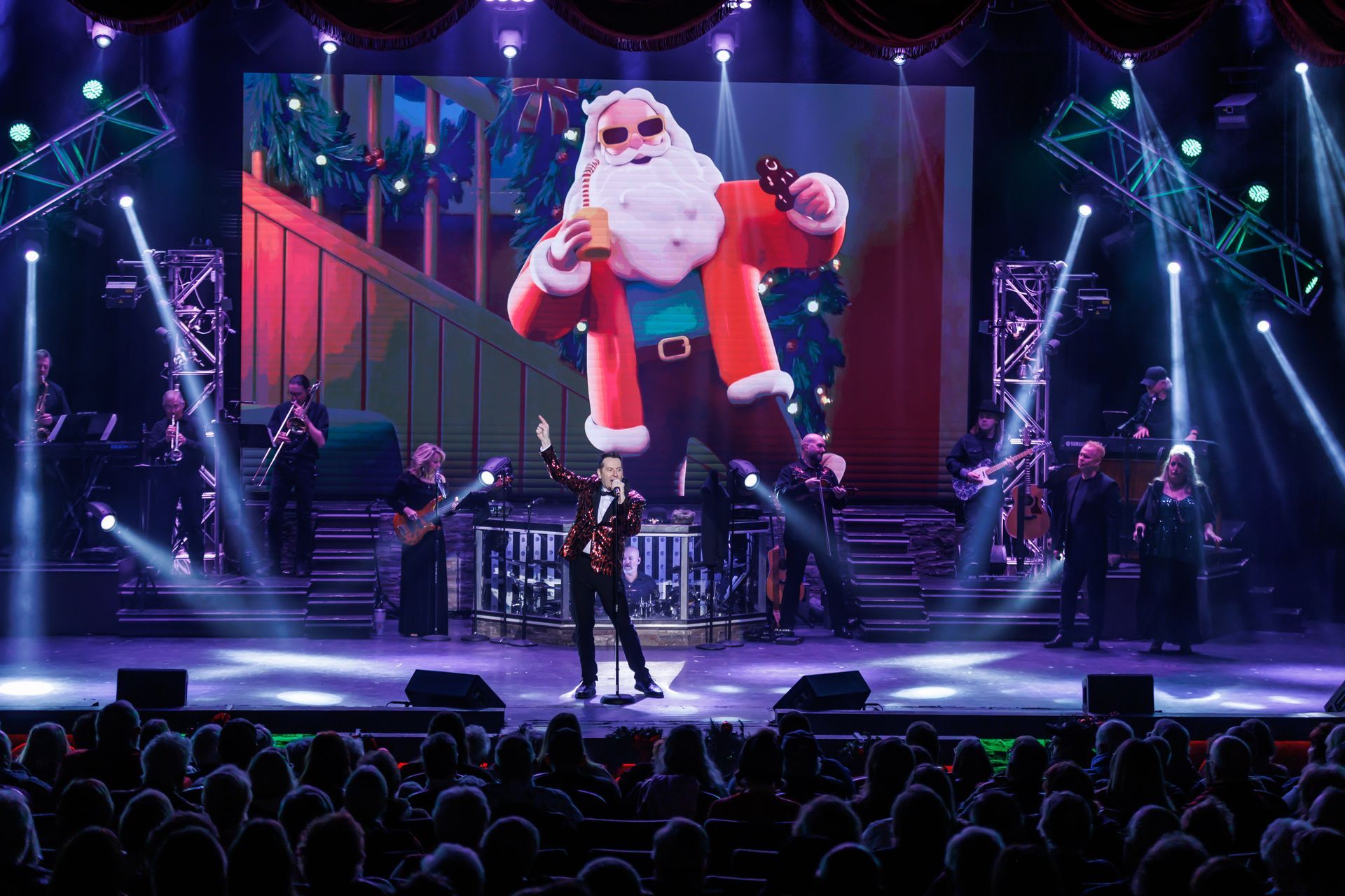 A singer performs on a stage in front of a large screen showing an animated Santa Claus holding a soda.