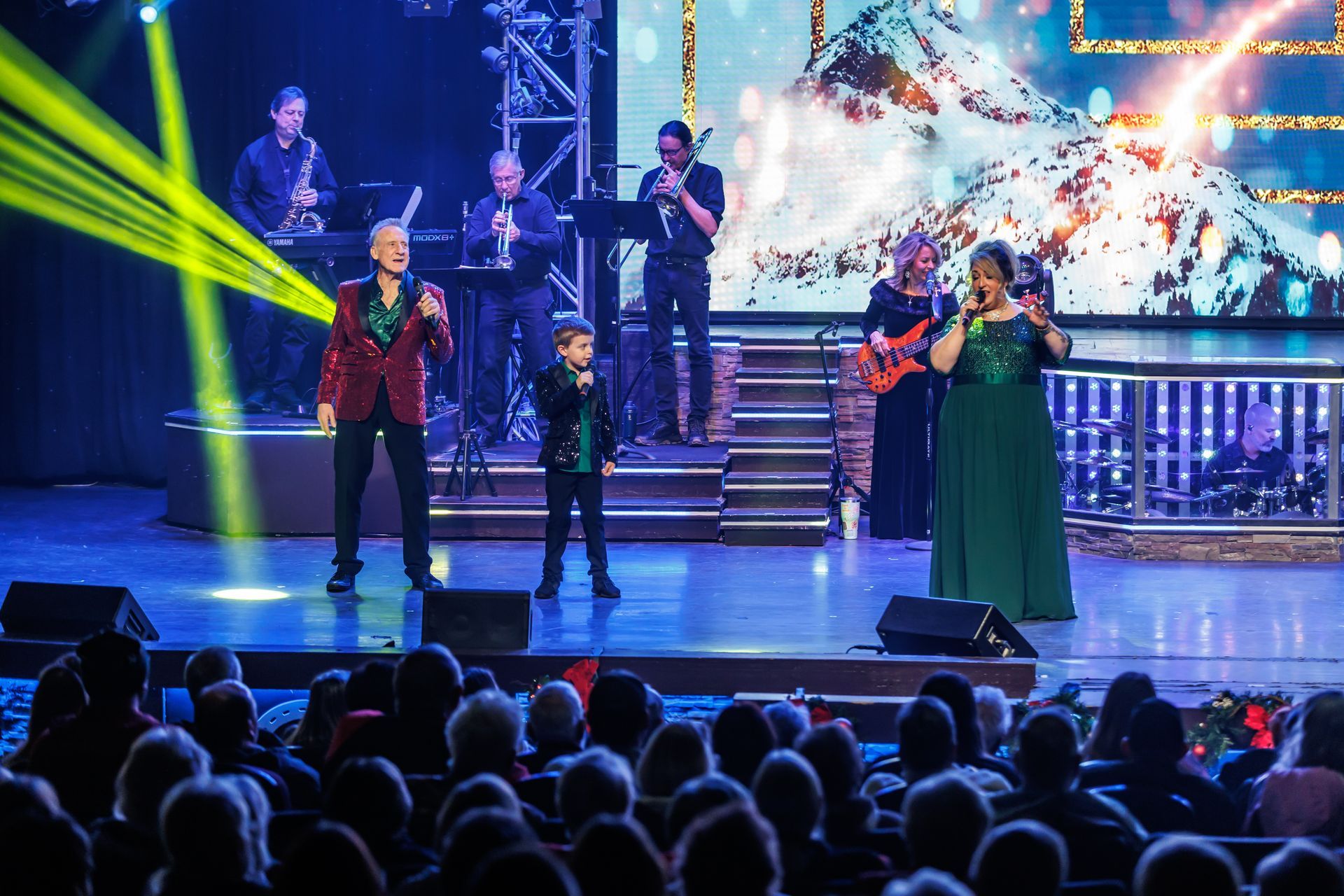 A musical ensemble performs on a brightly lit stage before a seated audience.