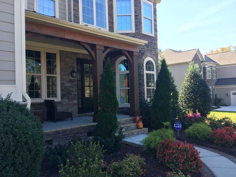 Front porch of a brick house with columns, large windows, and landscaped shrubs along a curved walkway