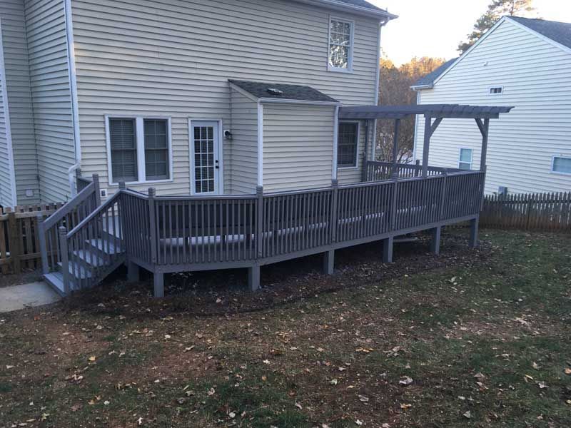 Wooden deck and ramp attached to a gray house in a backyard