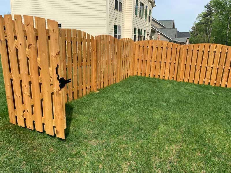 Wooden slat fence enclosing a grassy backyard beside a beige house on a sunny day