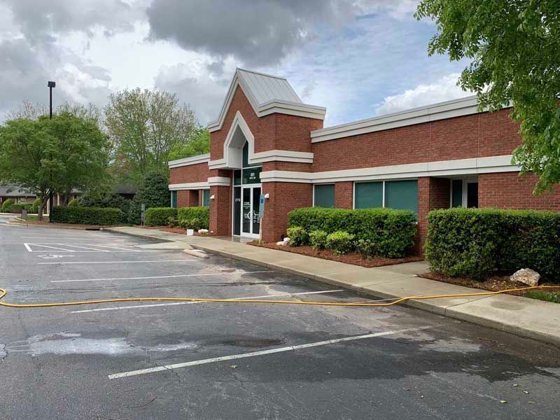 Empty parking lot outside a brick building with green windows and a white-trimmed entrance