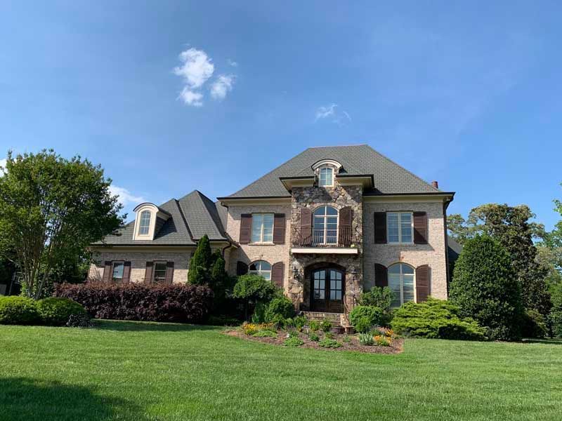 Large brick suburban house with a manicured lawn and blue sky above