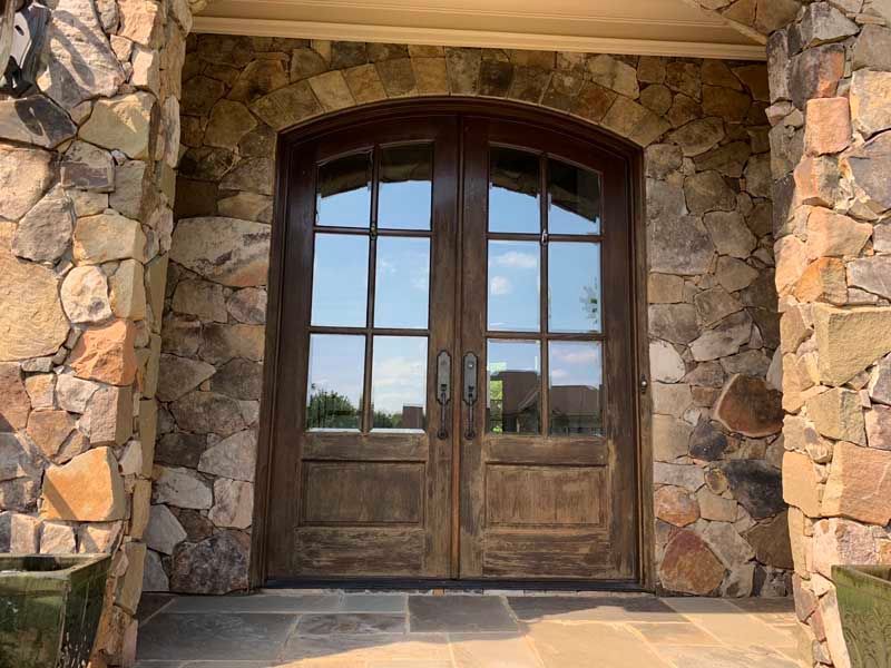 Wooden double front doors set in a stone entryway with arched glass panels