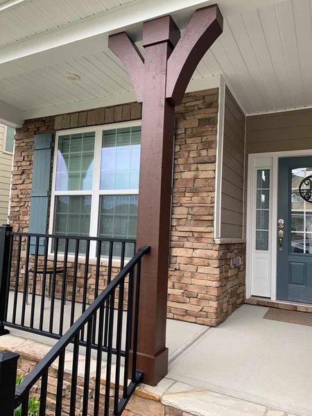 Front porch with stone column, black railing, and gray front door beside a window.