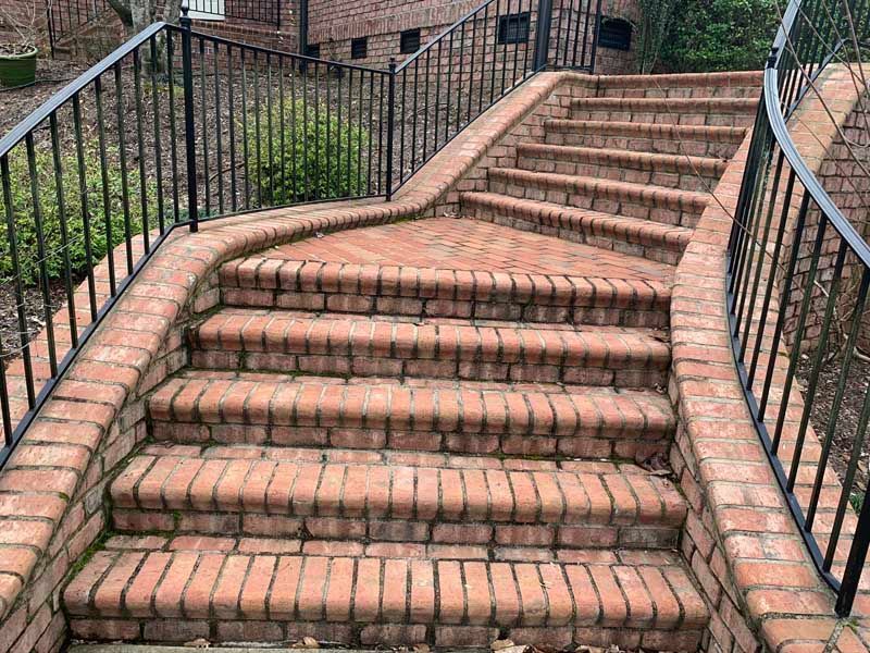 Brick outdoor staircase with black railings on both sides and a brick wall in the background