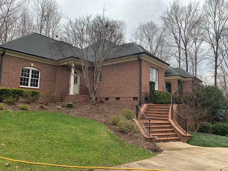 Brick house exterior with stairs, sloped lawn, and leafless trees