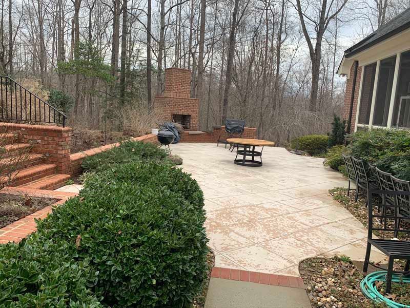 Backyard patio with brick steps, brick fireplace, patio furniture, and trees beyond.