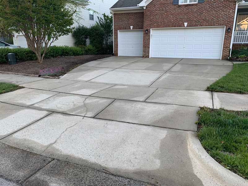 Cracked concrete driveway leading to a brick house with two white garage doors.