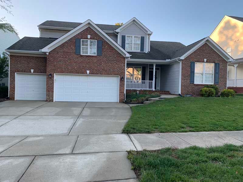 Suburban brick house with a three-car garage, driveway, and front lawn at dusk