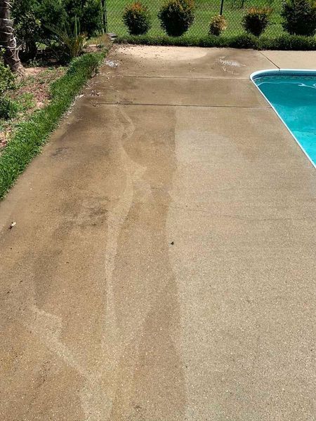 Poolside concrete walkway with a wet, stained section beside the blue pool