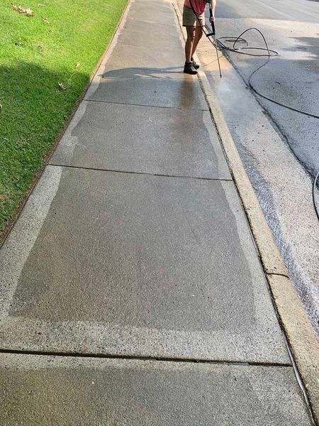 Sidewalk with a person walking away beside a grassy lawn and curb.