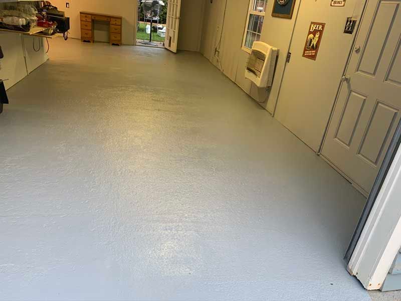 Indoor hallway with light gray floor, white walls, doors, and cabinets, viewed toward a back room.