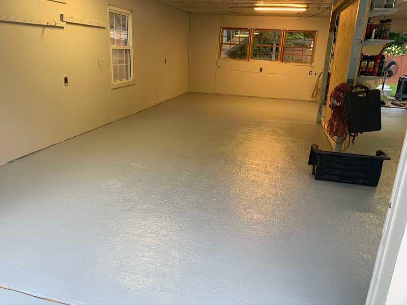 Empty garage with white floor and walls, windows at the back, and shelves along the right side