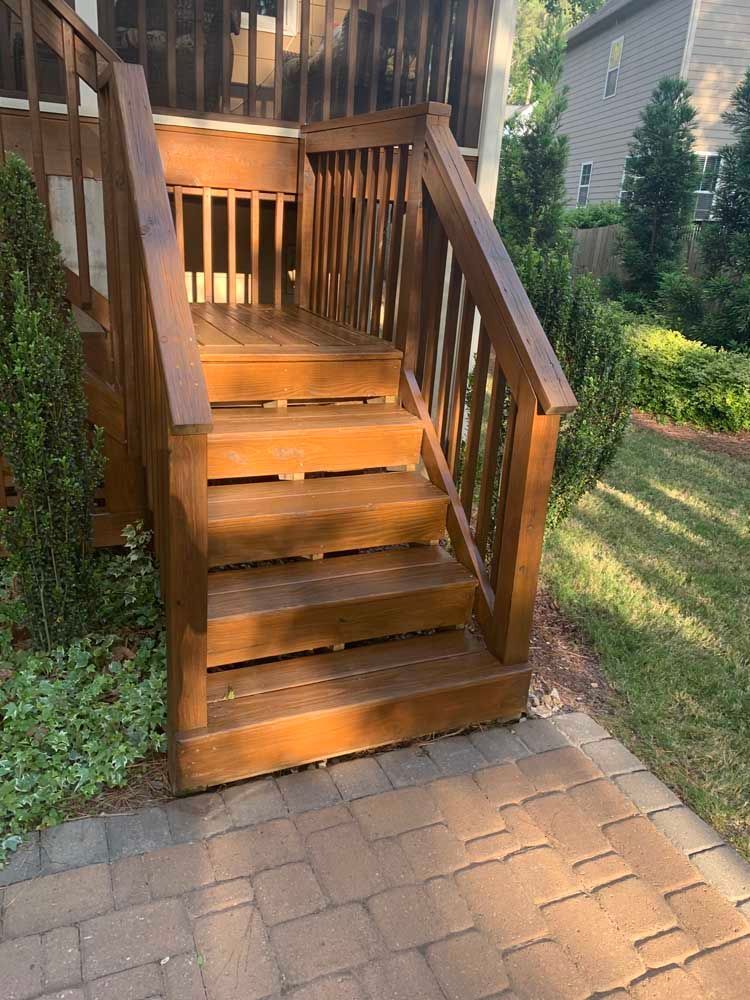 Wooden outdoor staircase with railings leading to a deck beside a paved path and greenery