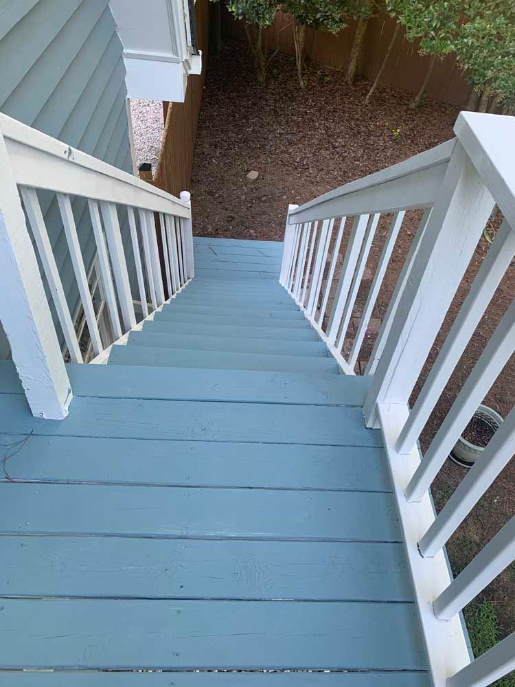 Top-down view of a blue-painted wooden staircase with white railings leading to a yard.