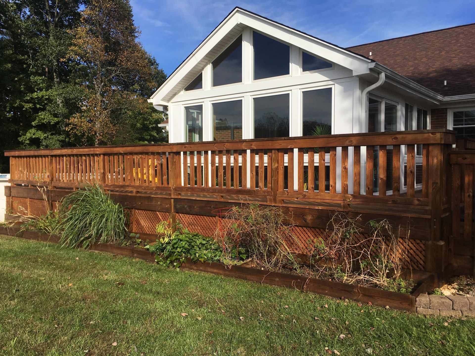 Wooden deck and railing in front of a white house with large windows and a sloped roof