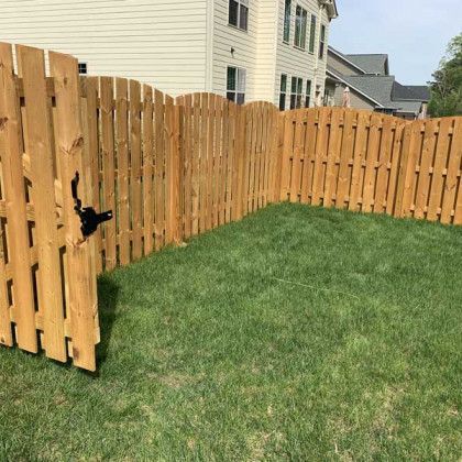 Wooden backyard fence with an open gate beside a green lawn and houses in the background