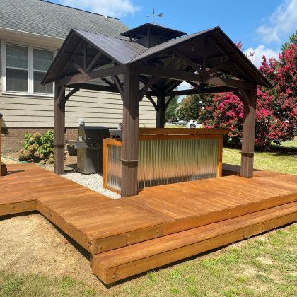 Wooden backyard deck with a gazebo, built-in bar, and surrounding landscaping