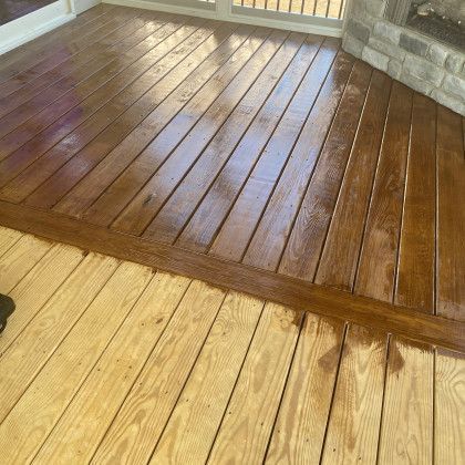 A wet dark-stained wooden deck beside a lighter unfinished wood floor and stone wall