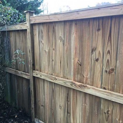 Weathered wooden fence with diagonal support beams and greenery behind it