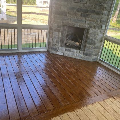Covered porch with a dark stained wooden floor and stone fireplace