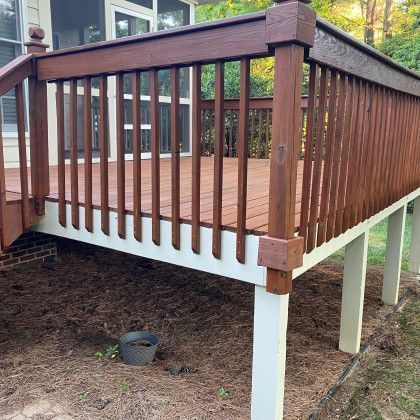 Wooden deck with brown railing and white support posts in a backyard