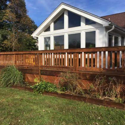 White house with large windows and wooden deck railing above a landscaped lawn and garden