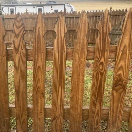 Wooden picket fence with pointed slats in front of a grassy yard and white RV in the background