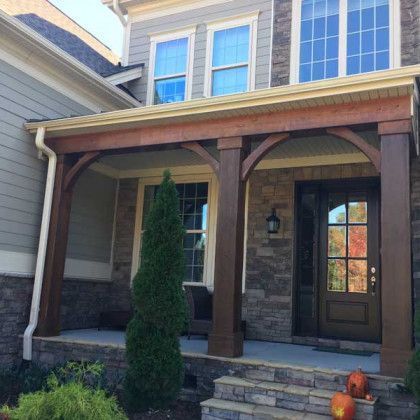 Front porch of a stone house with wooden columns, a dark front door, and steps with pumpkins.