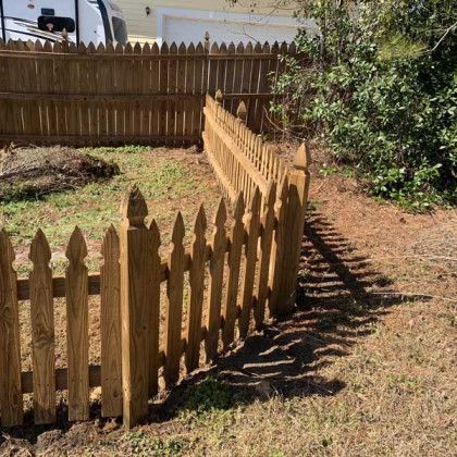 Curved wooden picket fence enclosing a small yard with grass and bushes in sunlight