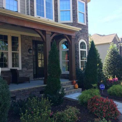 Front porch of a brick house with arched windows, shrubs, and flowers in the front yard