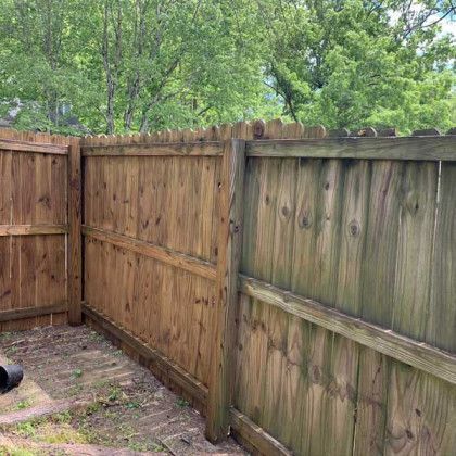 Wooden backyard fence corner with green trees visible above it