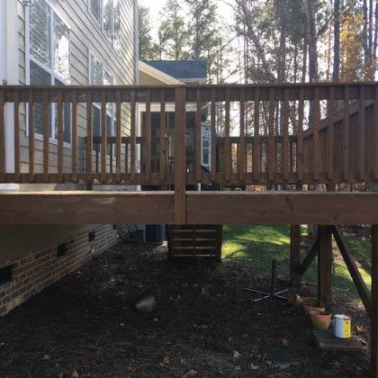 Wooden backyard deck attached to a house, with stairs and a shaded yard below.