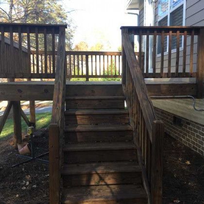 Wooden stairs leading to a raised deck with railings and a brick house exterior.