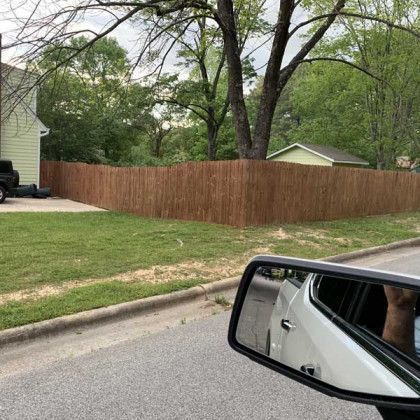 Quiet suburban street with a wooden fence, green lawn, and white car side mirror in the foreground