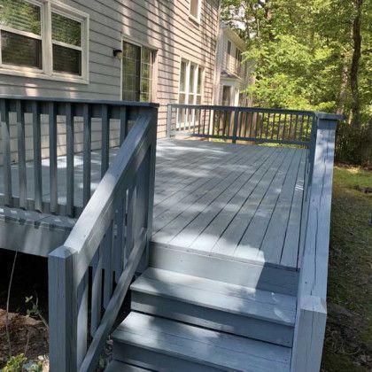Wooden deck with steps and railing beside a gray house in a wooded yard