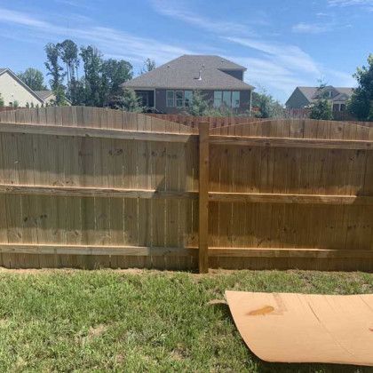 Backyard view with wooden fence, grass, and a cardboard piece on the lawn under a blue sky