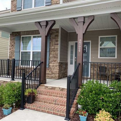 Front porch with brick steps, black railings, and columns at a townhouse entrance