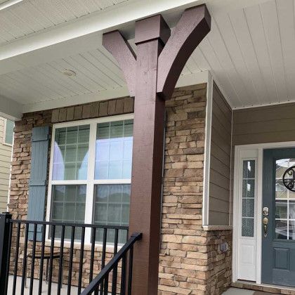 Front porch with stone columns, white siding ceiling, black railing, and a gray front door.