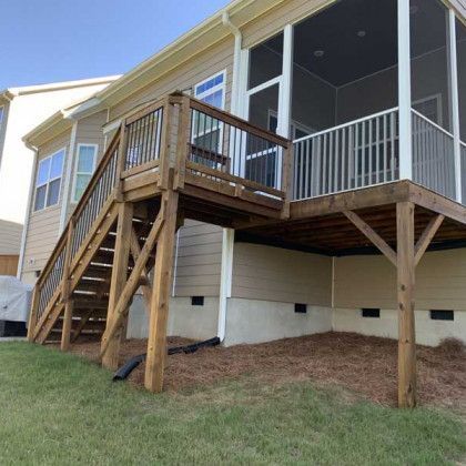 Raised wooden deck with stairs and railing on the back of a beige house