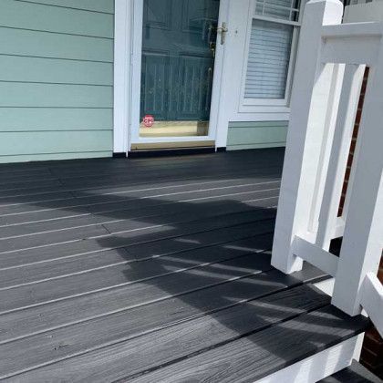 Front porch with dark composite decking, white railing, and a glass front door to a light blue house