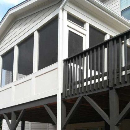 Raised house with white trim, dark screened porch, and gray deck railing on stilts
