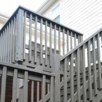 Gray wooden staircase and deck railing beside a house exterior
